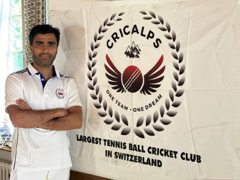 A player in a white club polo standing with arms folded beside the Cricalps banner