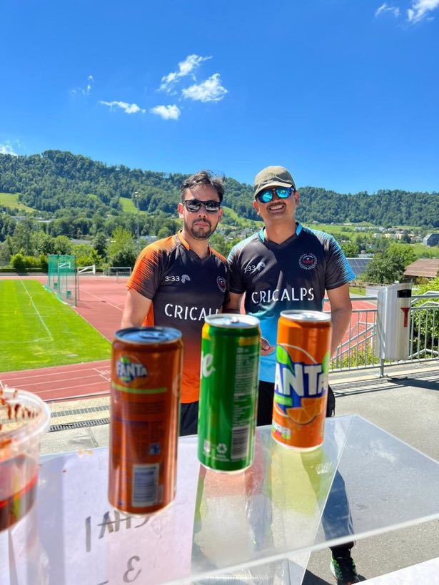 Two players in club kit on a sunny terrace above the ground, drinks on the ledge in front of them