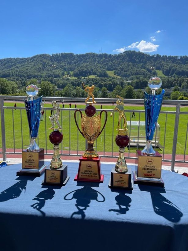 Two tall blue winners trophies on a table, green hills beyond the railing