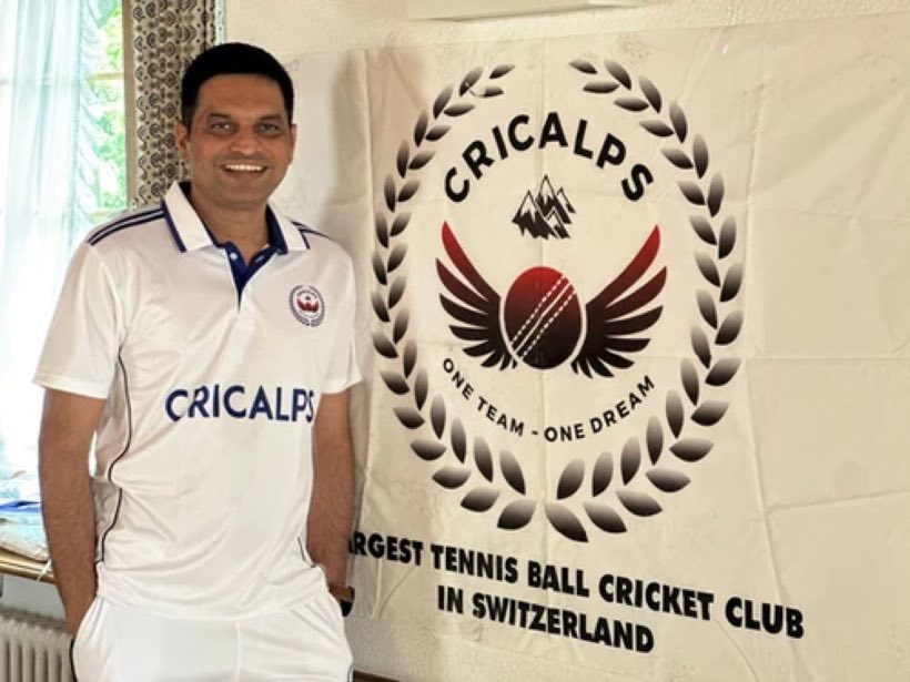 A smiling player in club whites beside the Cricalps banner