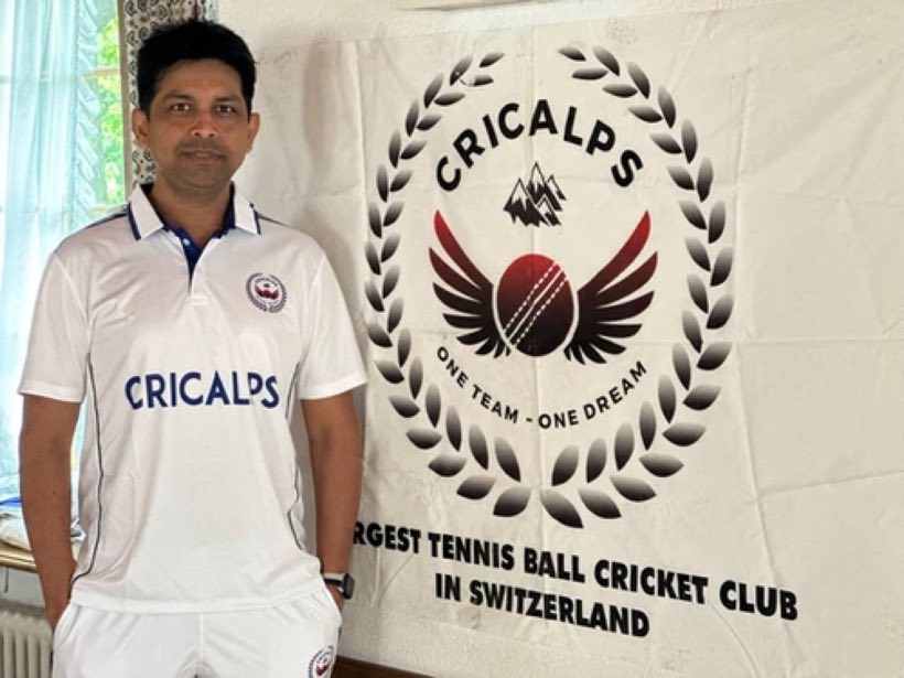 A player in the white Cricalps shirt in front of the club banner