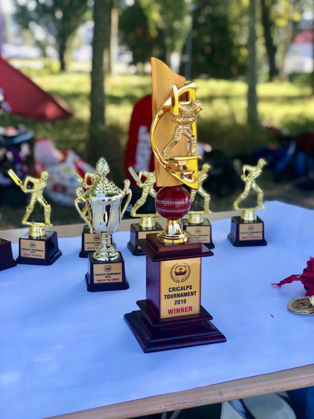 A row of trophies and a large winners cup on a blue presentation table