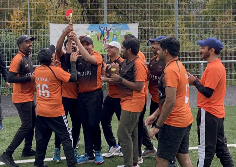 The orange side raising a trophy together in front of the tournament board
