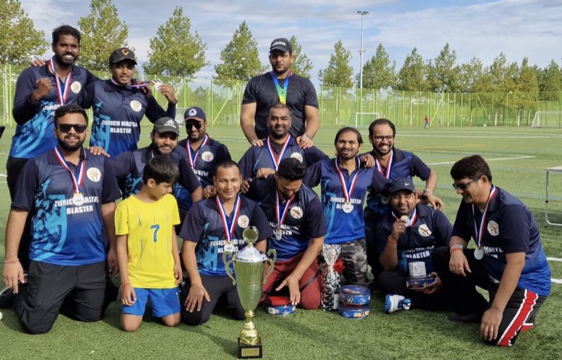 A large group with medals around their necks and a trophy in front, children among them